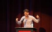 A man raises his arms while talking from a podium.